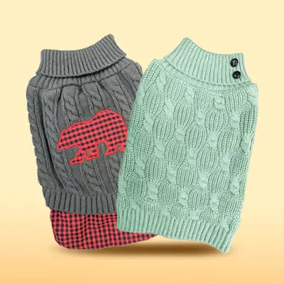 Two dog sweaters, one gray with a red and black checkered bear design, the other green with a textured pattern, on a beige background.
